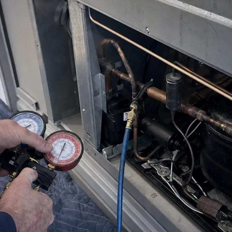 Technician holding refrigerant gauges beside an open compressor bay with copper lines and a blue hose.